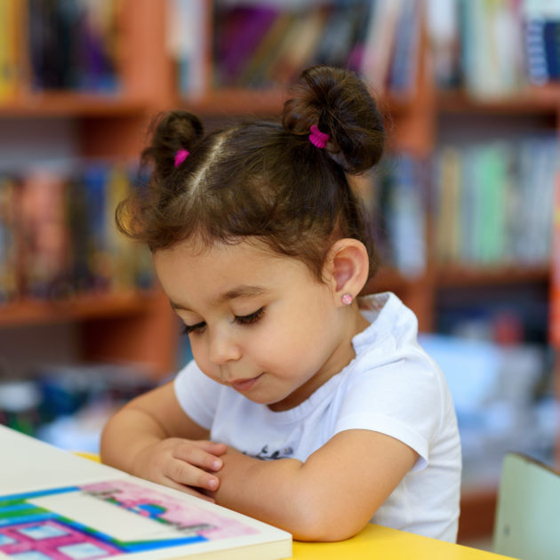 Una niña pequeña leyendo un libro en una biblioteca.